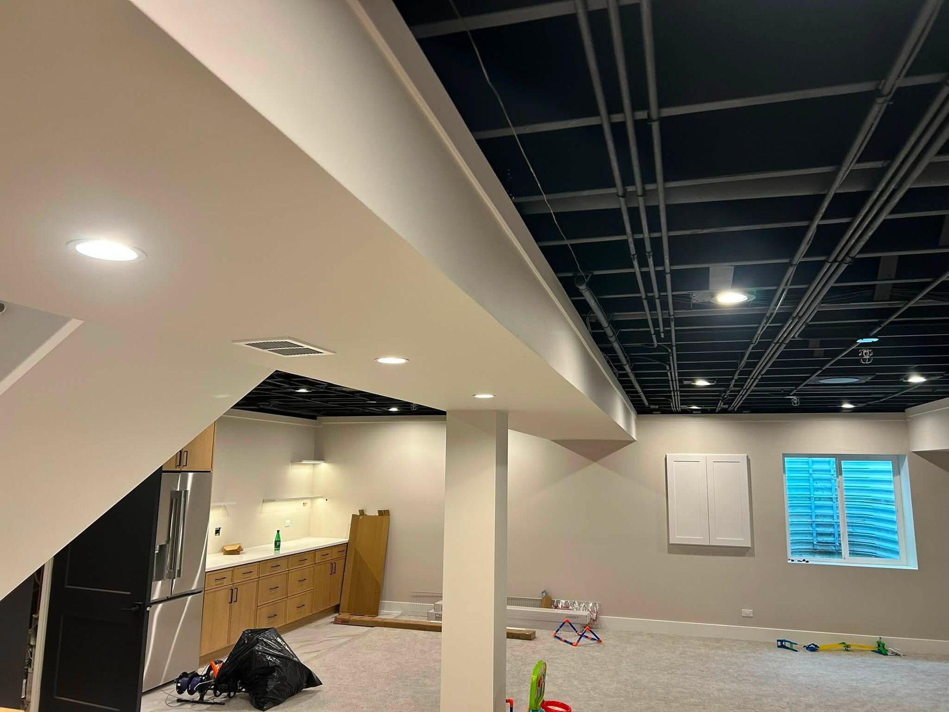 Basement with unfinished ceiling, white walls, and scattered tools and debris during renovation