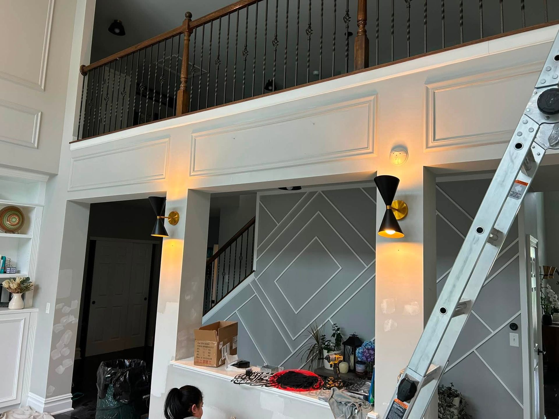 Interior with tall accent wall, wall sconces, ladder, and a mezzanine railing in a modern room.