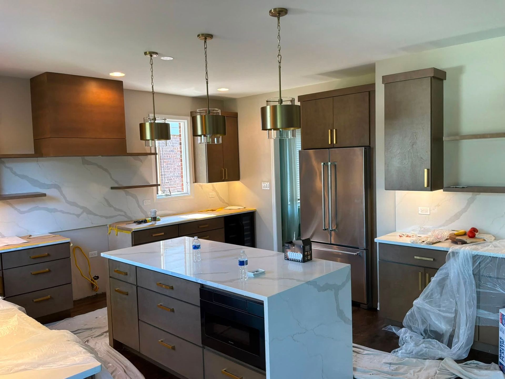 Modern kitchen with white island, wood cabinets, stainless fridge, and marble backsplash under pendant lights