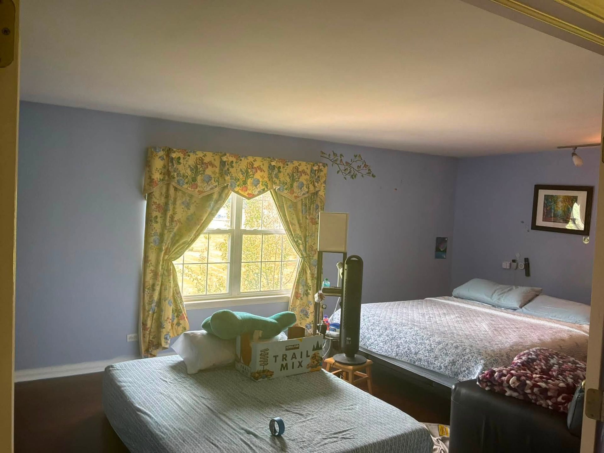 Bedroom with lavender walls, two beds, a window with yellow curtains, and a TV near the center.