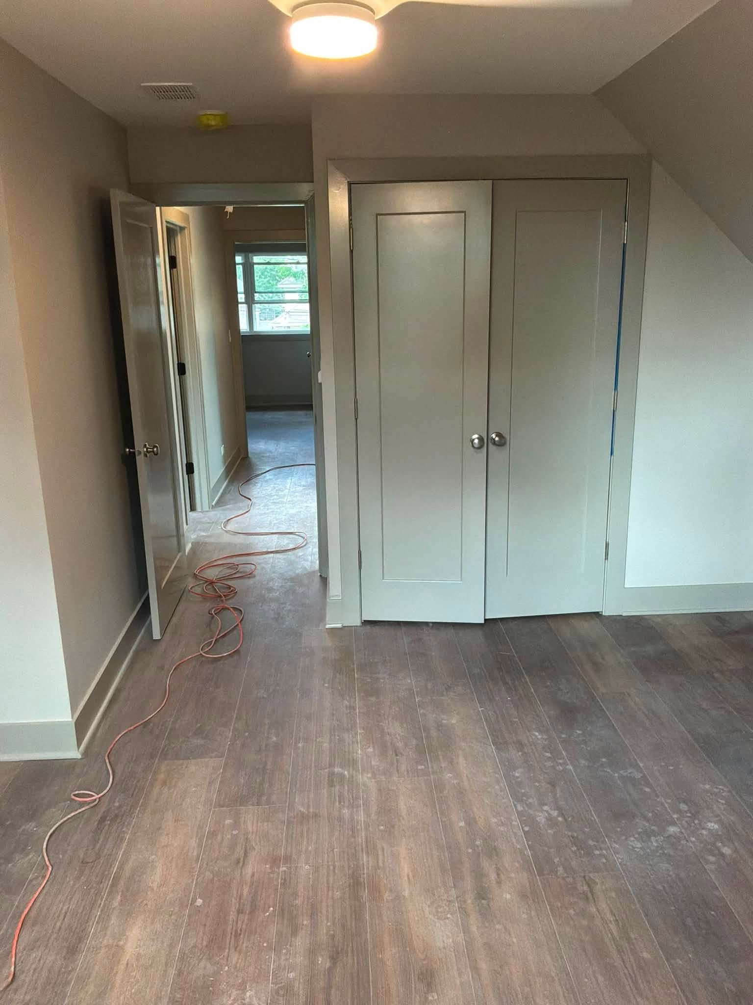 Empty hallway with gray walls, wood floor, and closed white closet doors, lit by a ceiling light.