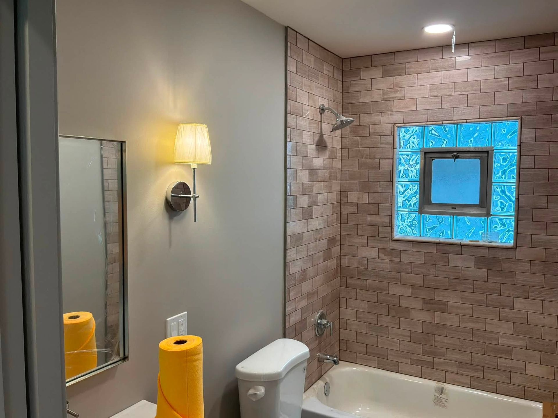 Small bathroom with white vanity, toilet, tub, brick tile shower, and blue-lit mirror area
