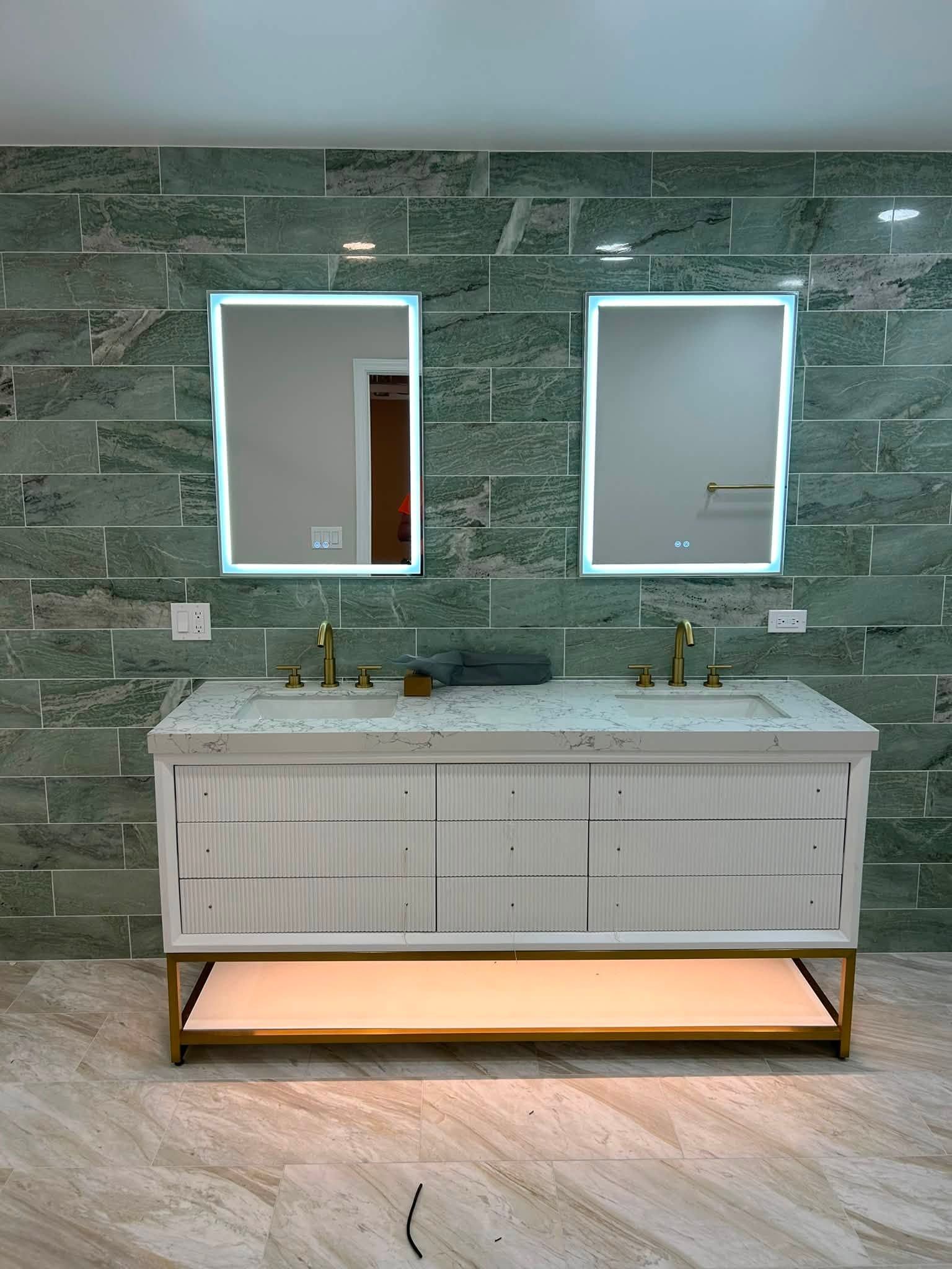 Double vanity bathroom sink with two mirrors, green marble wall, and soft under-cabinet lighting.