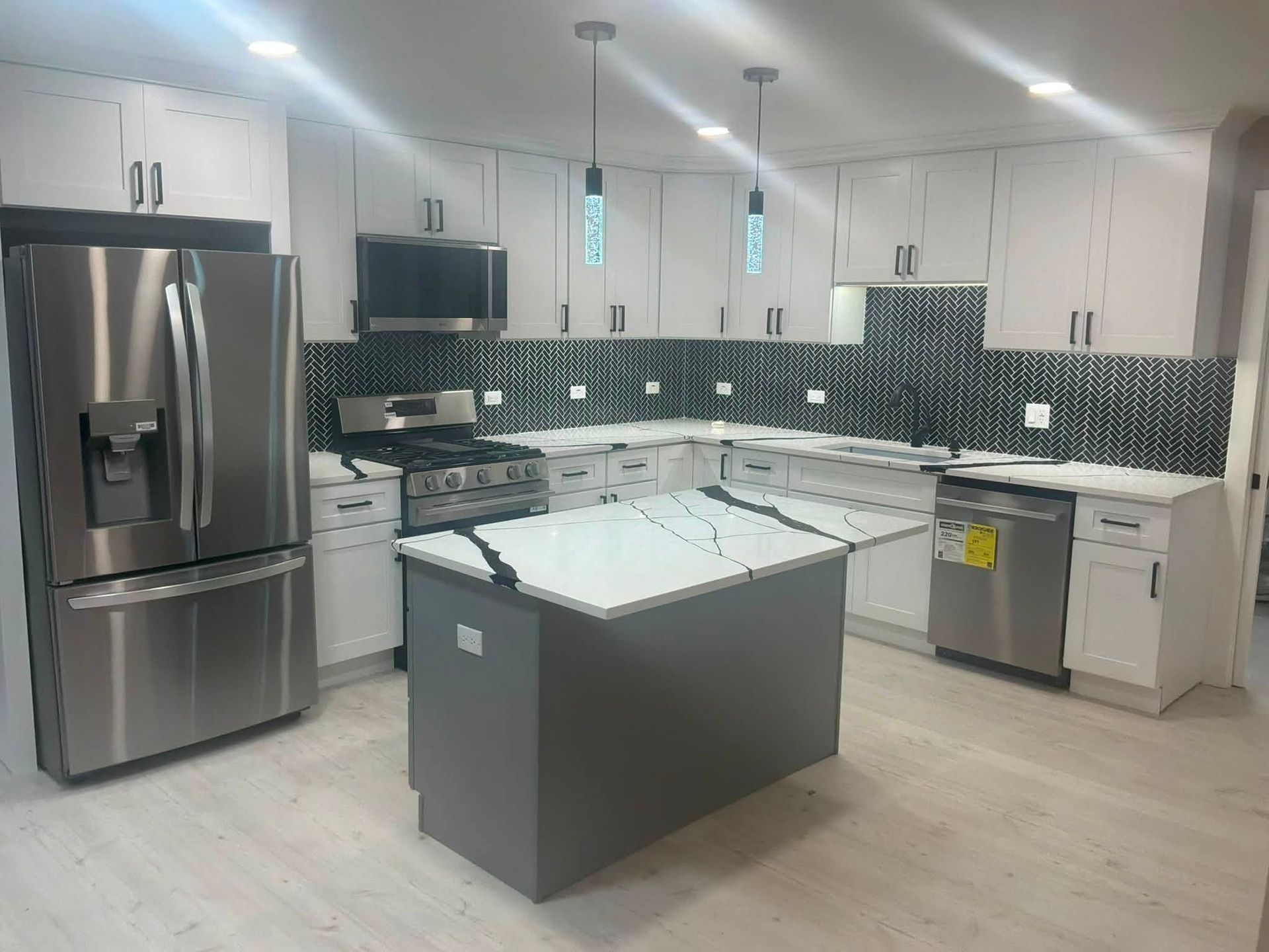 Modern kitchen with stainless steel appliances, white cabinets, mosaic backsplash, and central island.