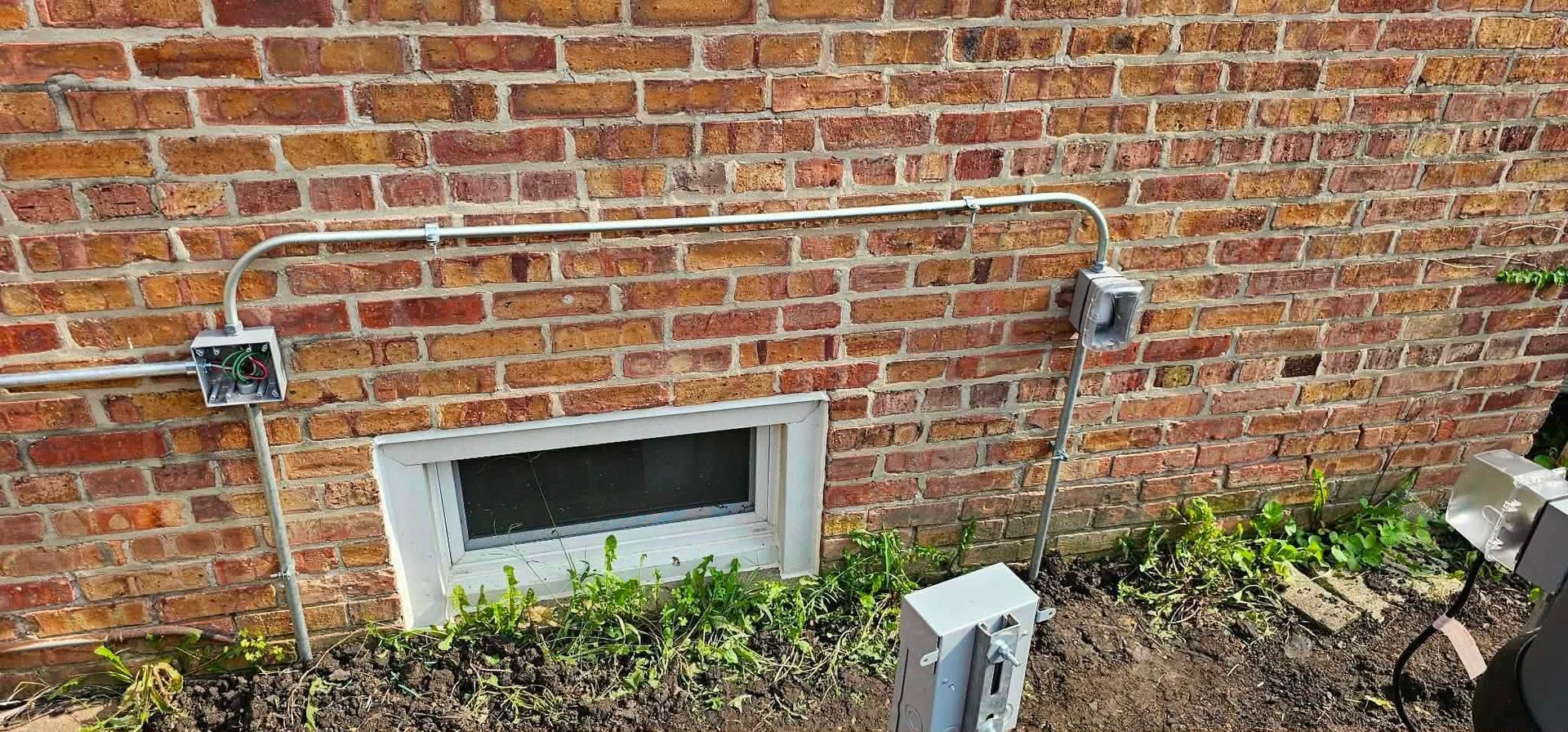 Brick house exterior with a small basement window, wall vent, and utility boxes near the ground