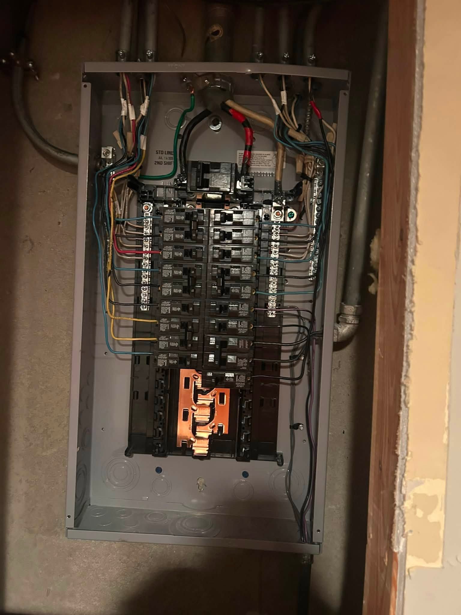 Open electrical breaker panel with exposed wiring in a wall cavity