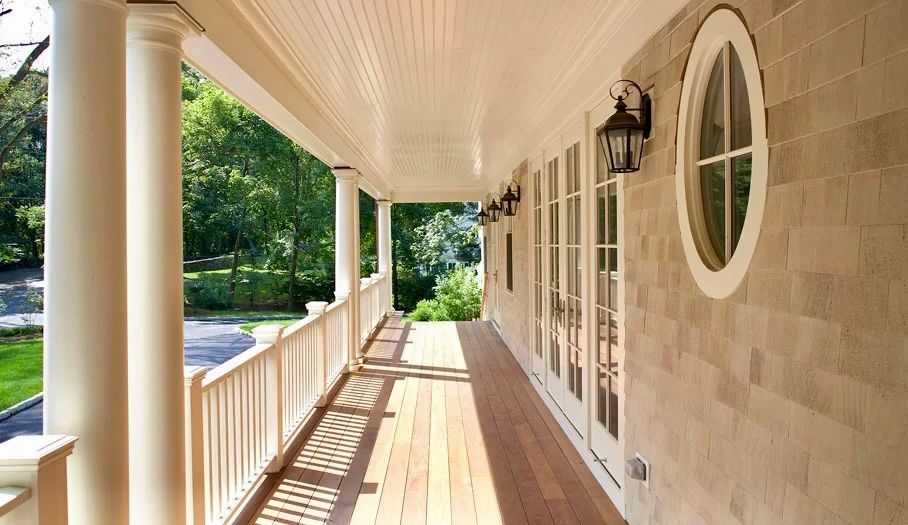 Exterior porch with white columns, wood deck, and light-colored shingles.
