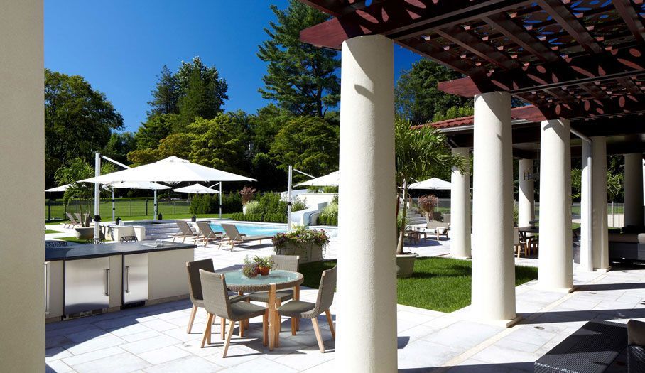 Outdoor patio with columns, pool, umbrellas, and dining area on a sunny day.