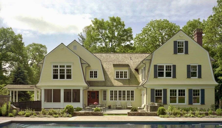 Yellow house with blue shutters and a pool on a sunny day.