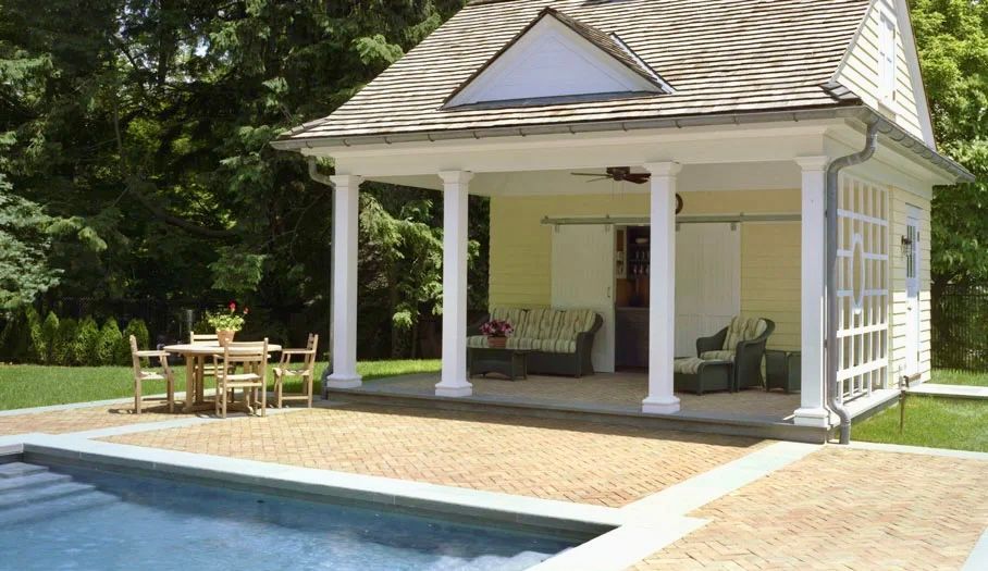 Poolside cabana with brick patio, seating, and columns.