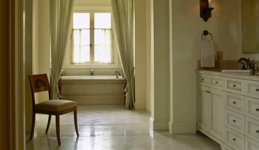 Elegant bathroom with a bathtub under a window, chair, and white vanity.