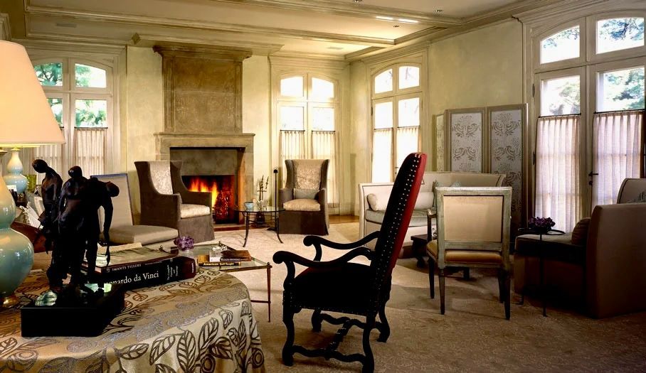 Elegant living room with fireplace, ornate furniture, and large windows. Warm lighting and neutral colors.