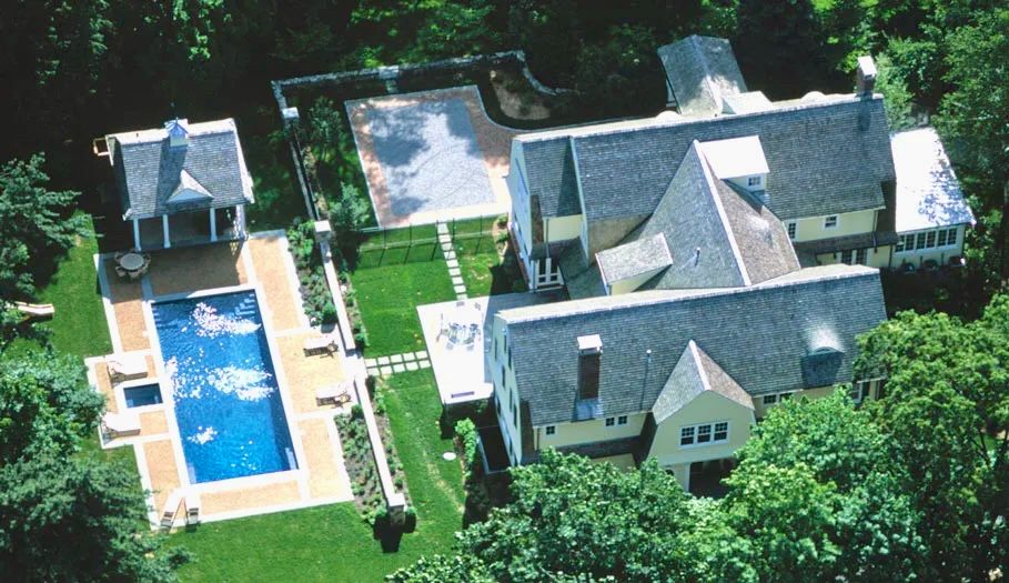 Aerial view of a large yellow house with a pool, gazebo, and manicured lawn surrounded by trees.