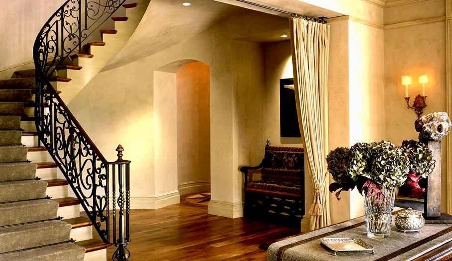 Elegant staircase with wrought iron railing. Beige walls, wood floors, entry bench, and floral arrangement.