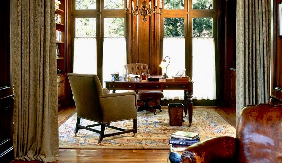 A wood-paneled office with a desk, chair, and large windows with cream-colored blinds.