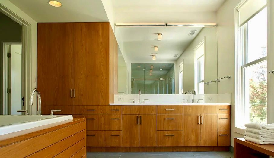 Modern bathroom with wooden cabinets, large mirror, and white countertop.