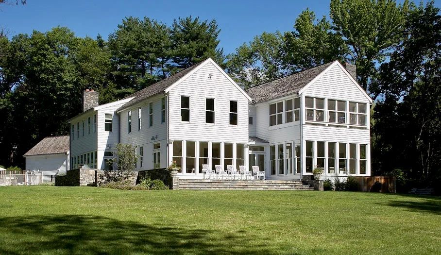 White house with many windows and lawn, trees in background.