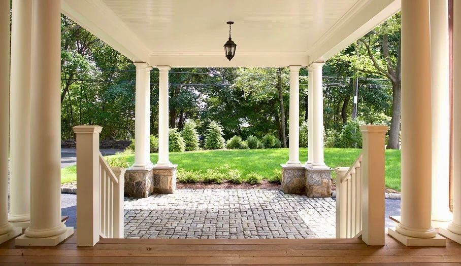 Covered porch with white columns, stone path, stairs, and view of green lawn and trees.