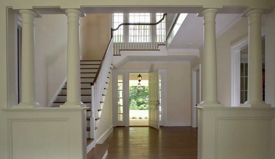 Interior entryway with white pillars, staircase, and open doorway to outdoor greenery.