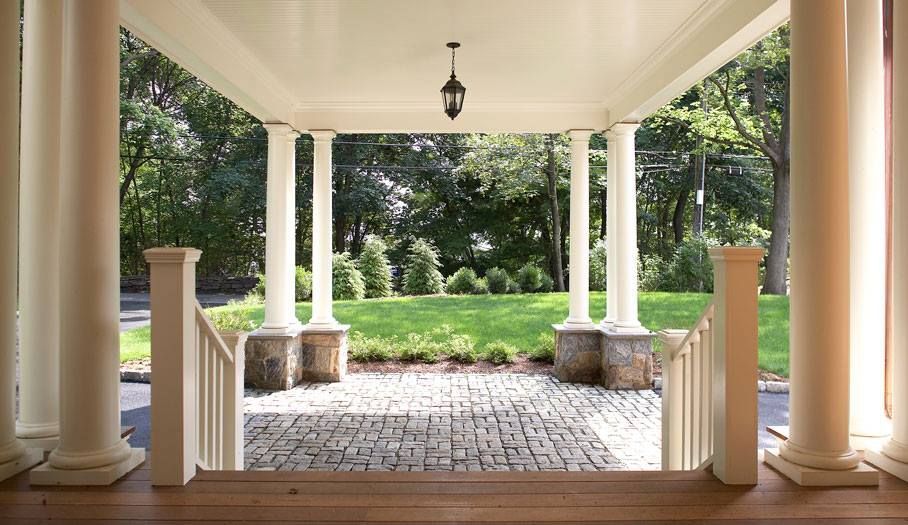 Covered porch with white columns, steps, and a brick patio leading to a grassy yard and trees.