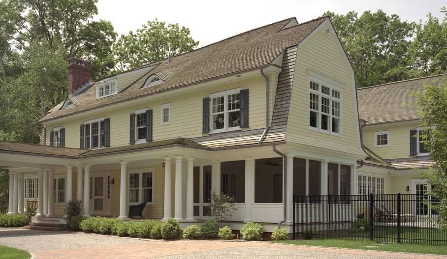 Yellow two-story house with porch and black shutters, on a brick driveway.