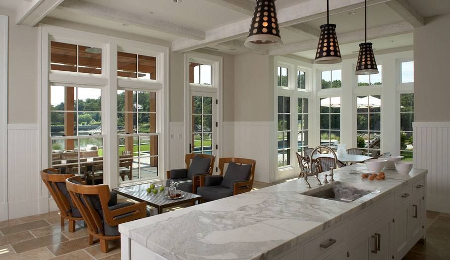 Spacious white kitchen with marble island, large windows, and outdoor seating.