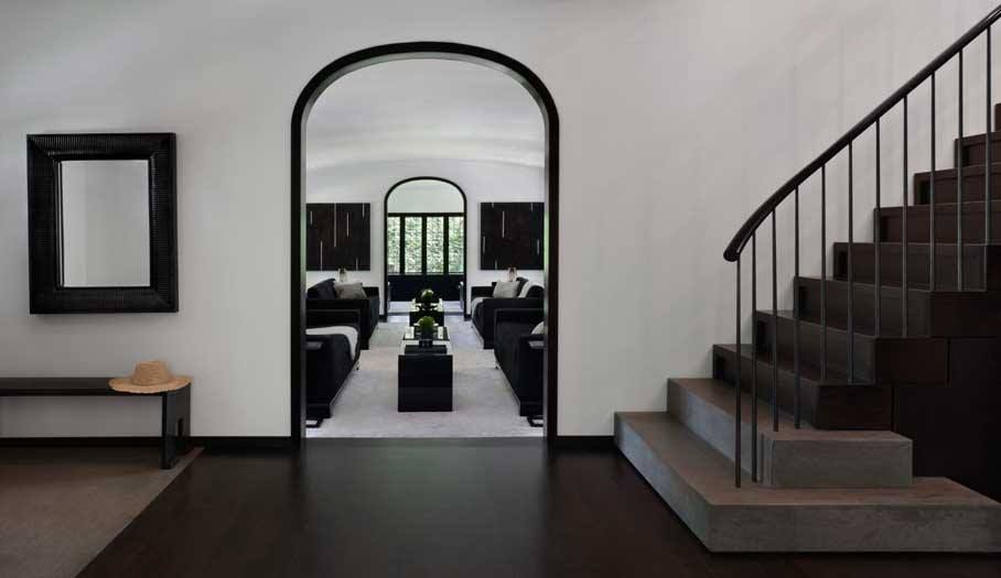 Interior of a home with an arched doorway, dark flooring, and a staircase. Black and white color scheme.