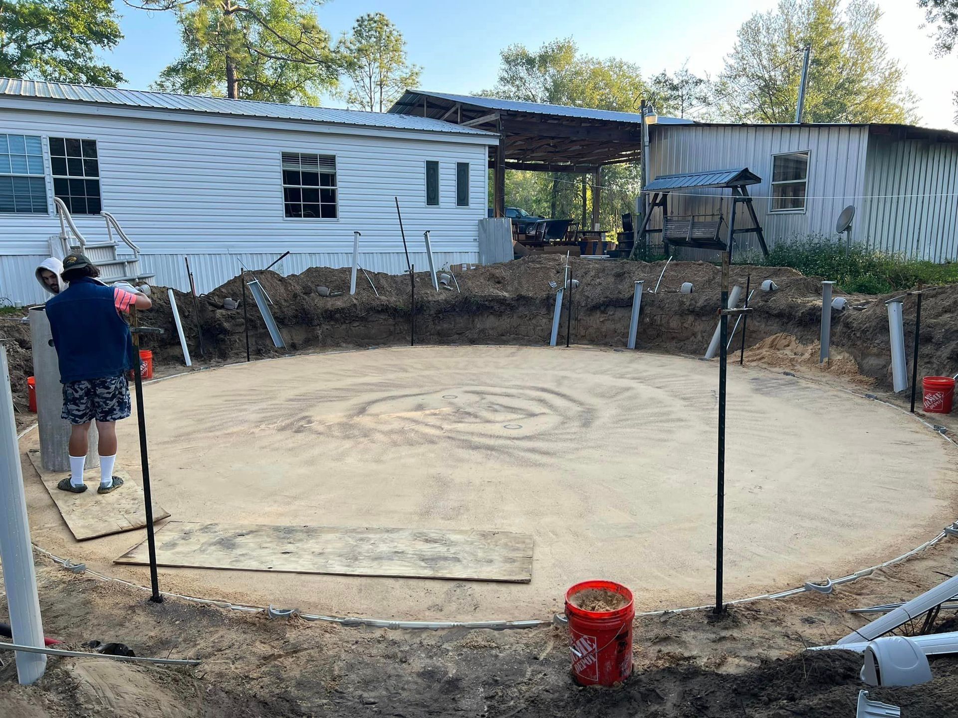 A man is standing in the dirt in front of a mobile home.
