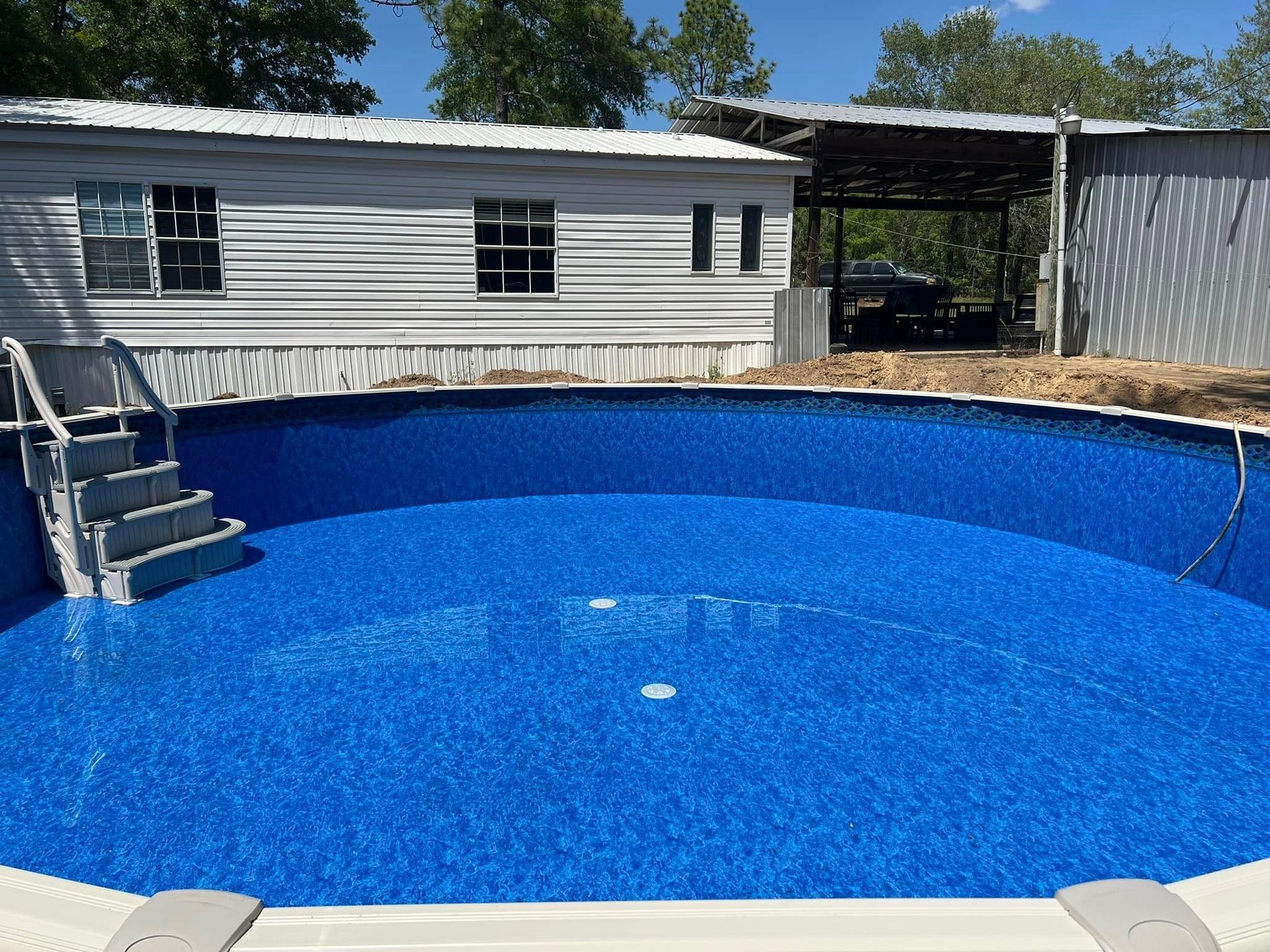 A blue swimming pool with stairs in front of a mobile home.
