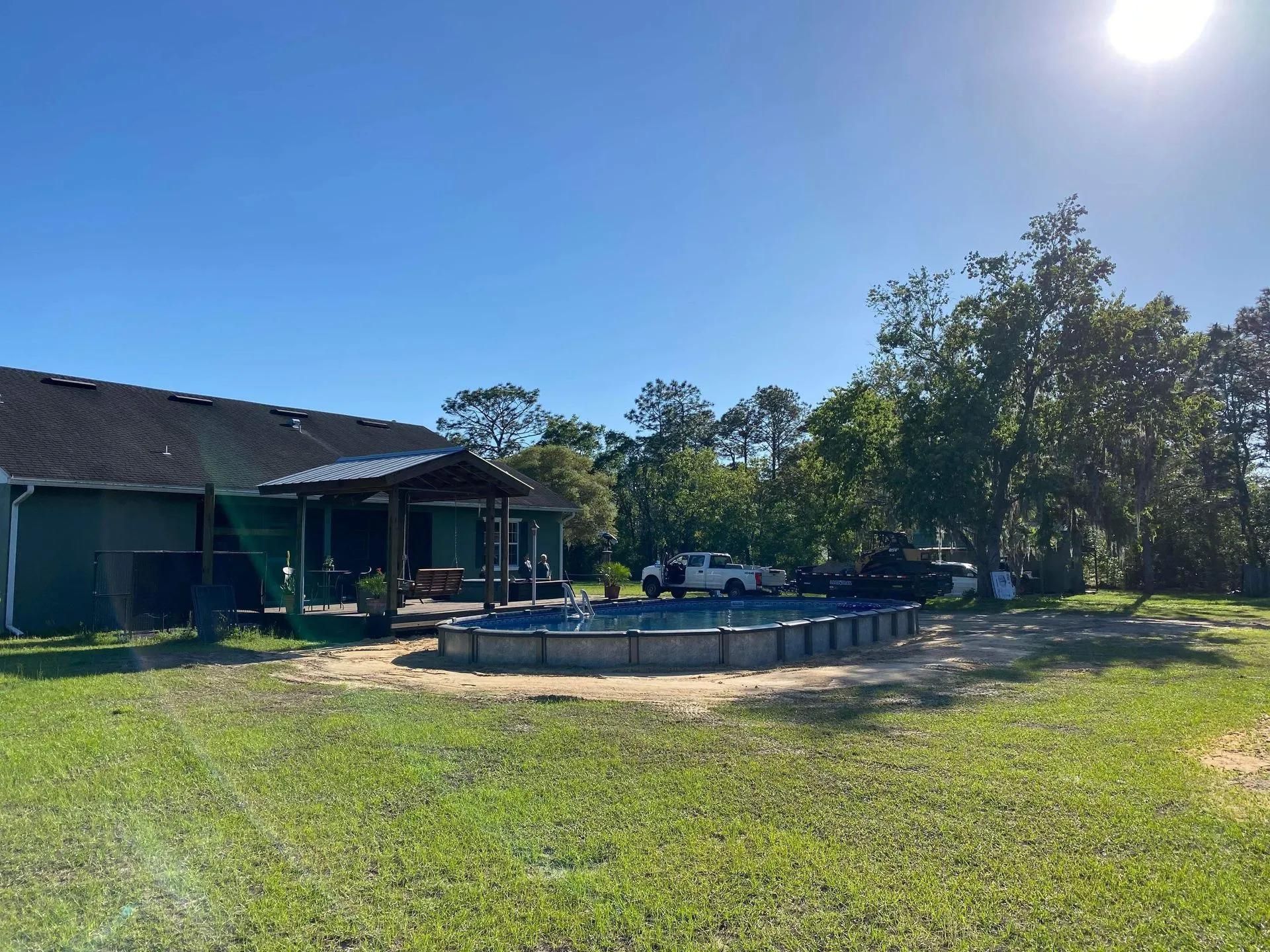 A large swimming pool is in the middle of a lush green field in front of a house.