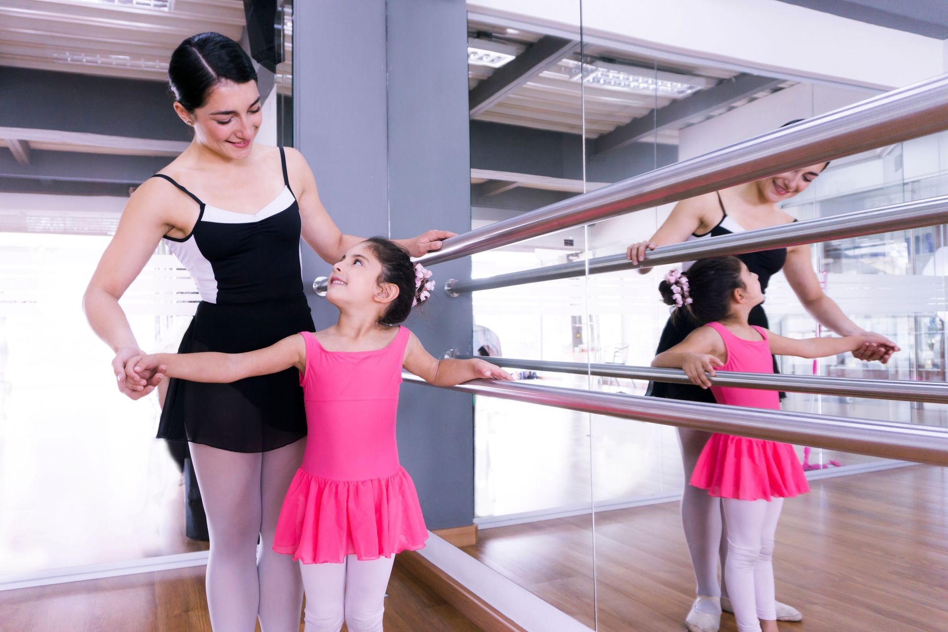 Ballet instructor holding a young dancer’s hands in a studio with mirrors and a barre