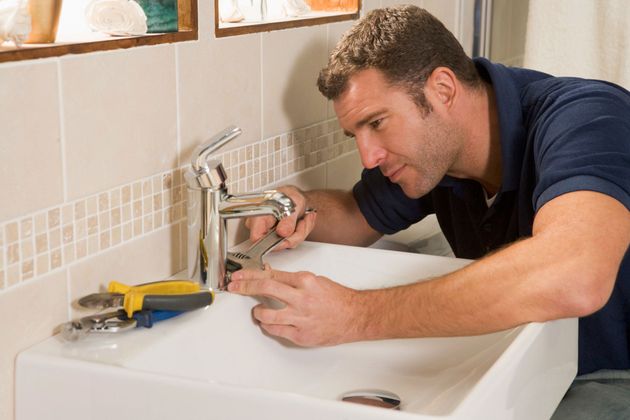 Man repairing a bathroom sink faucet with tools on the counter