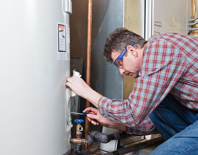 Technician inspecting a water heater and plumbing in a utility room