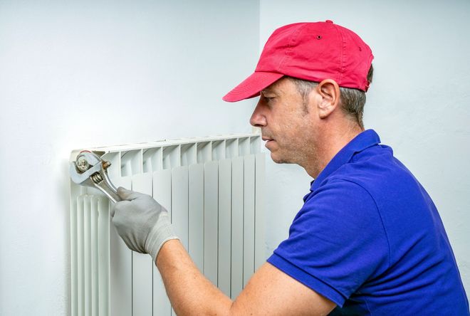 Technician in blue shirt and red cap adjusting a white radiator with a wrench