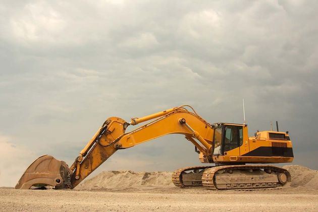 Yellow excavator digging on a sandy construction site under a cloudy sky