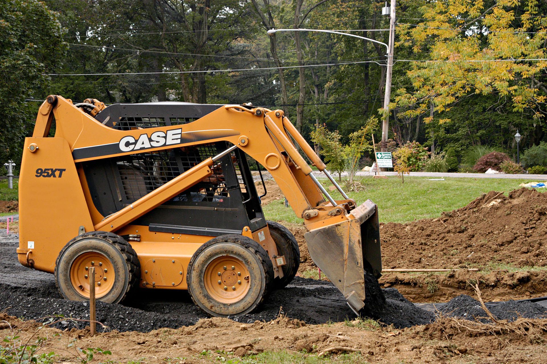 Yellow CASE skid-steer loader digging dirt beside a muddy roadside with a soil pile behind it