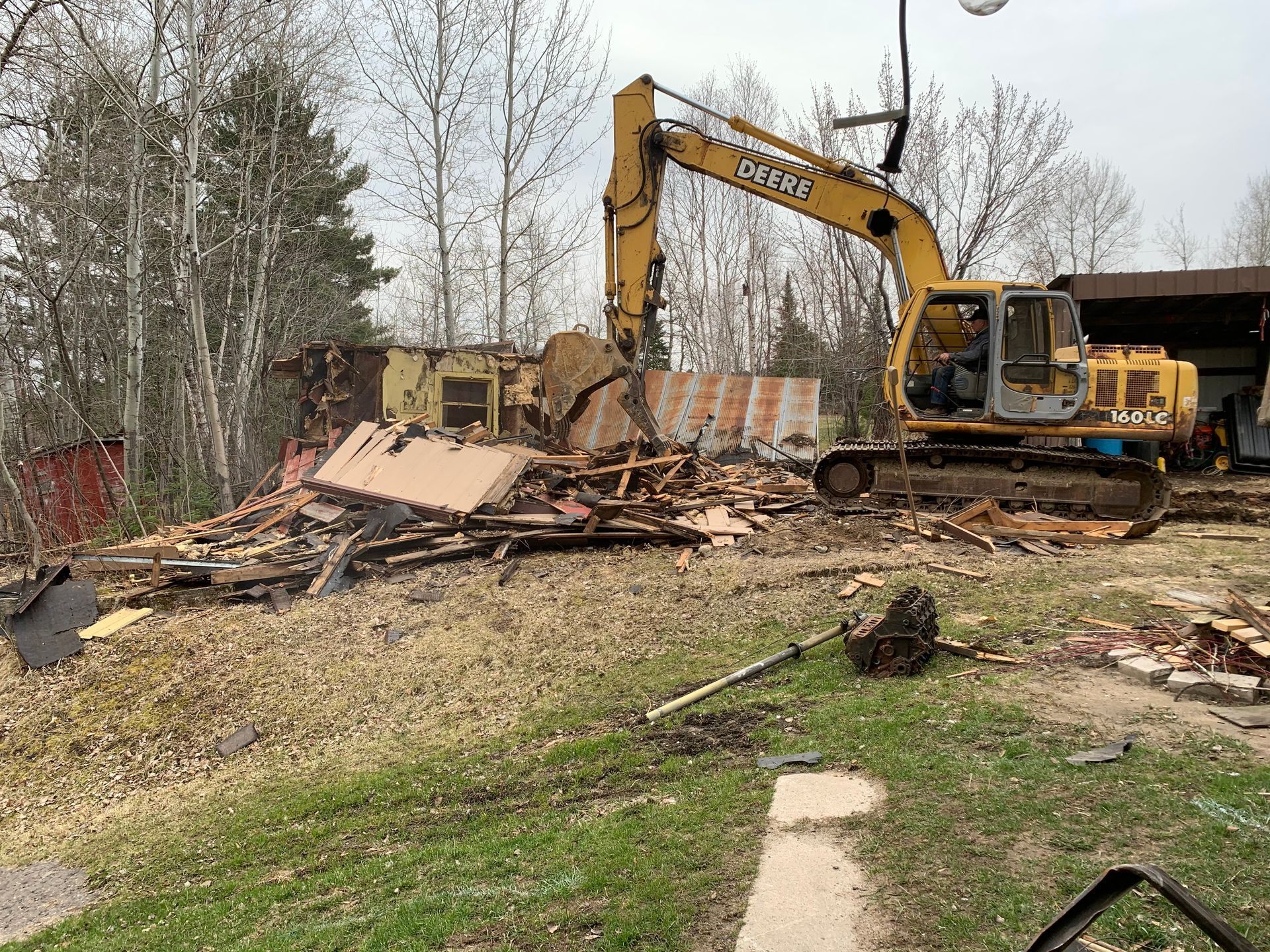 A large yellow excavator is demolishing a building in a yard.