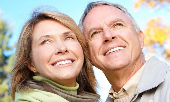 Smiling couple outdoors, wrapped in scarves, looking up at the sky.