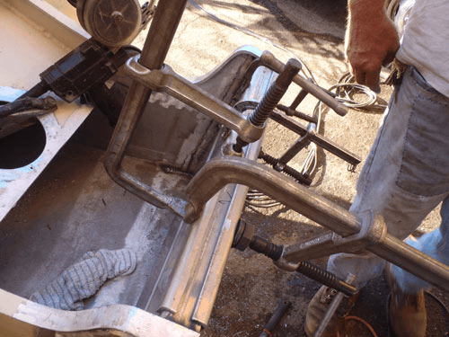 A man is working on a piece of metal with a clamp.
