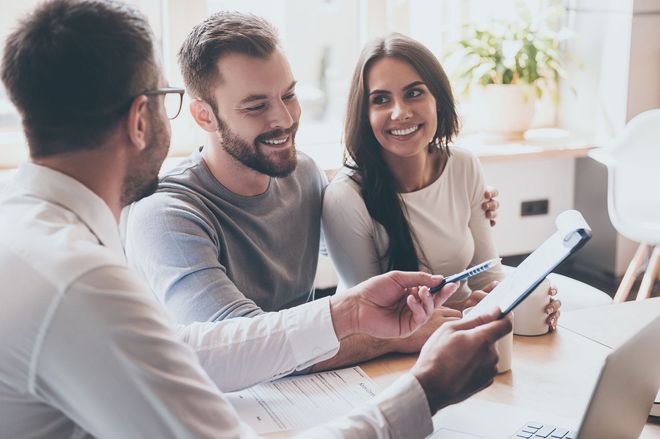 Three people smiling and discussing a tablet in a bright office