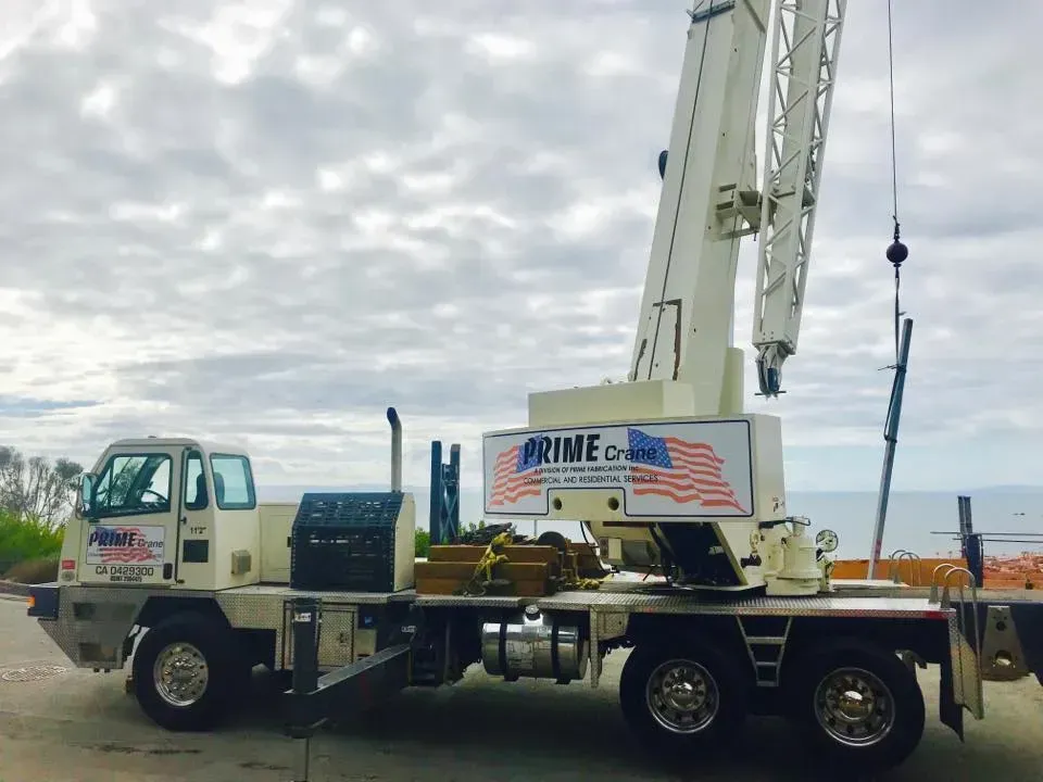 Crane truck with raised boom on the coast. White and blue truck, cloudy sky.