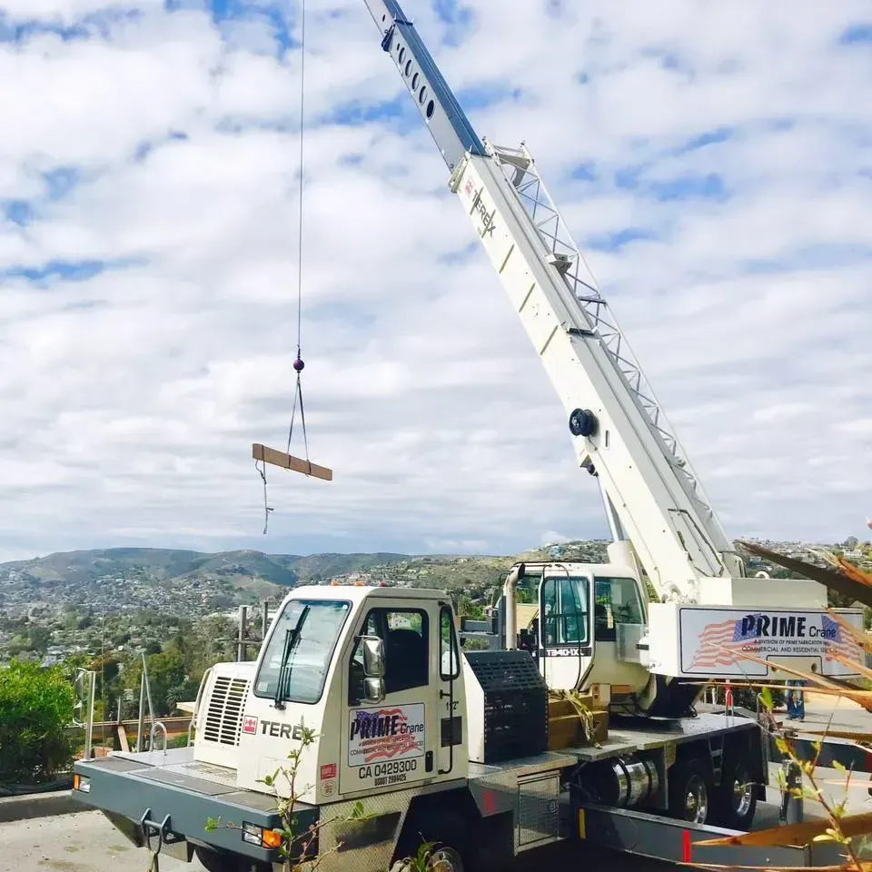 Crane lifting lumber on a construction site overlooking a hilly landscape. The crane is white.