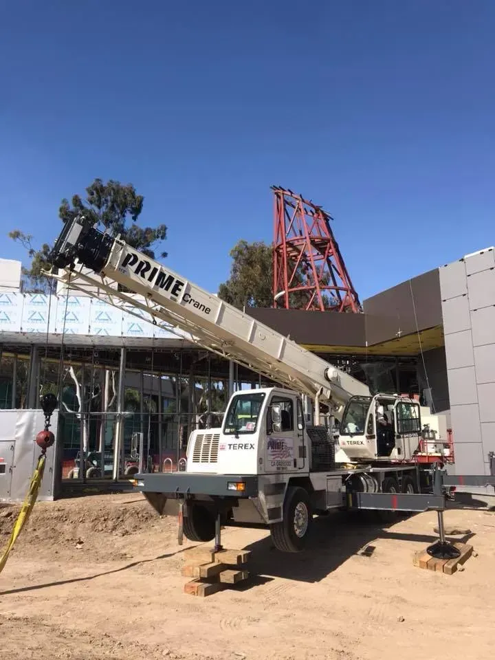 A crane with an extended boom on a construction site; building under construction in the background.
