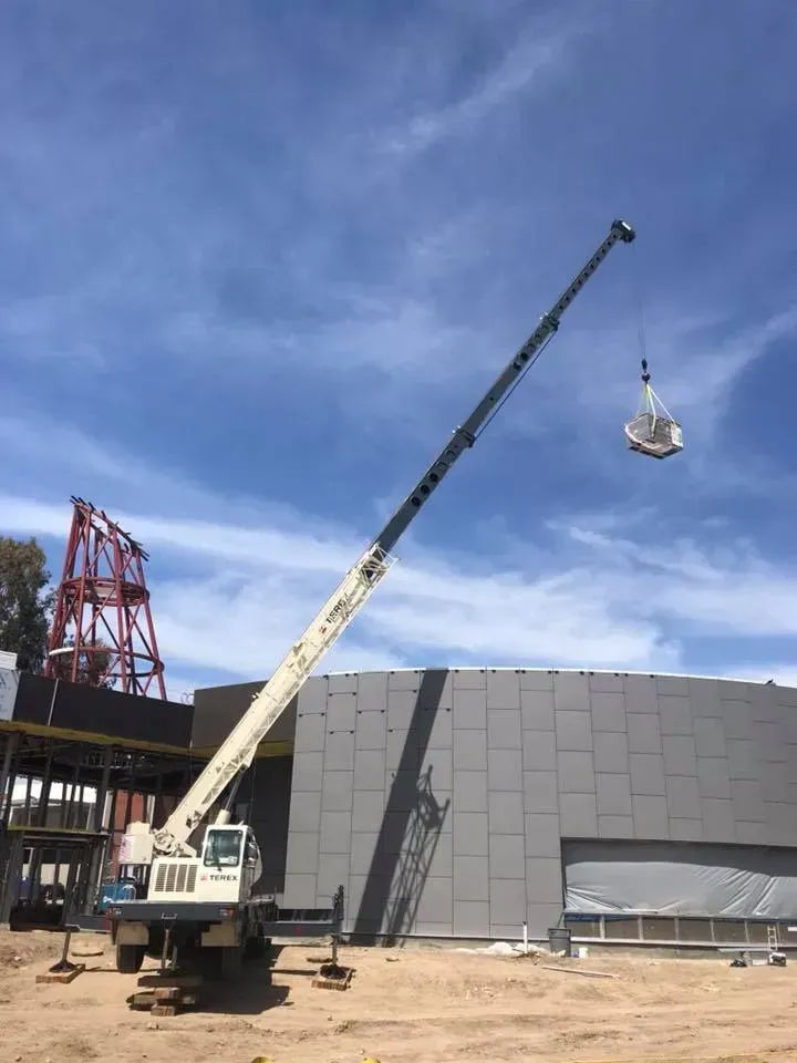 A large crane lifting a wrapped object near a building under construction on a sunny day.