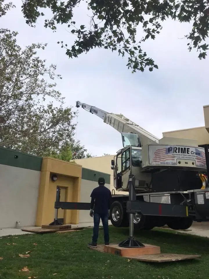 A crane lifting something near a building; a person is observing on a grassy area.