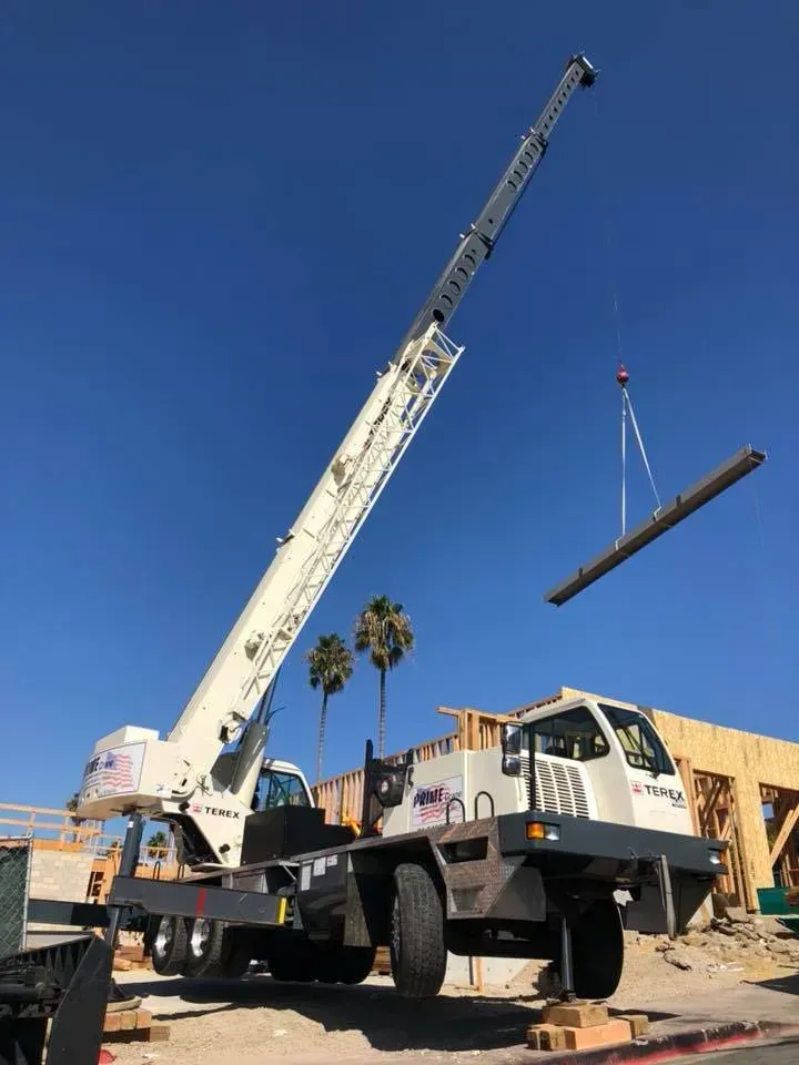 Crane lifting a beam at a construction site on a sunny day.