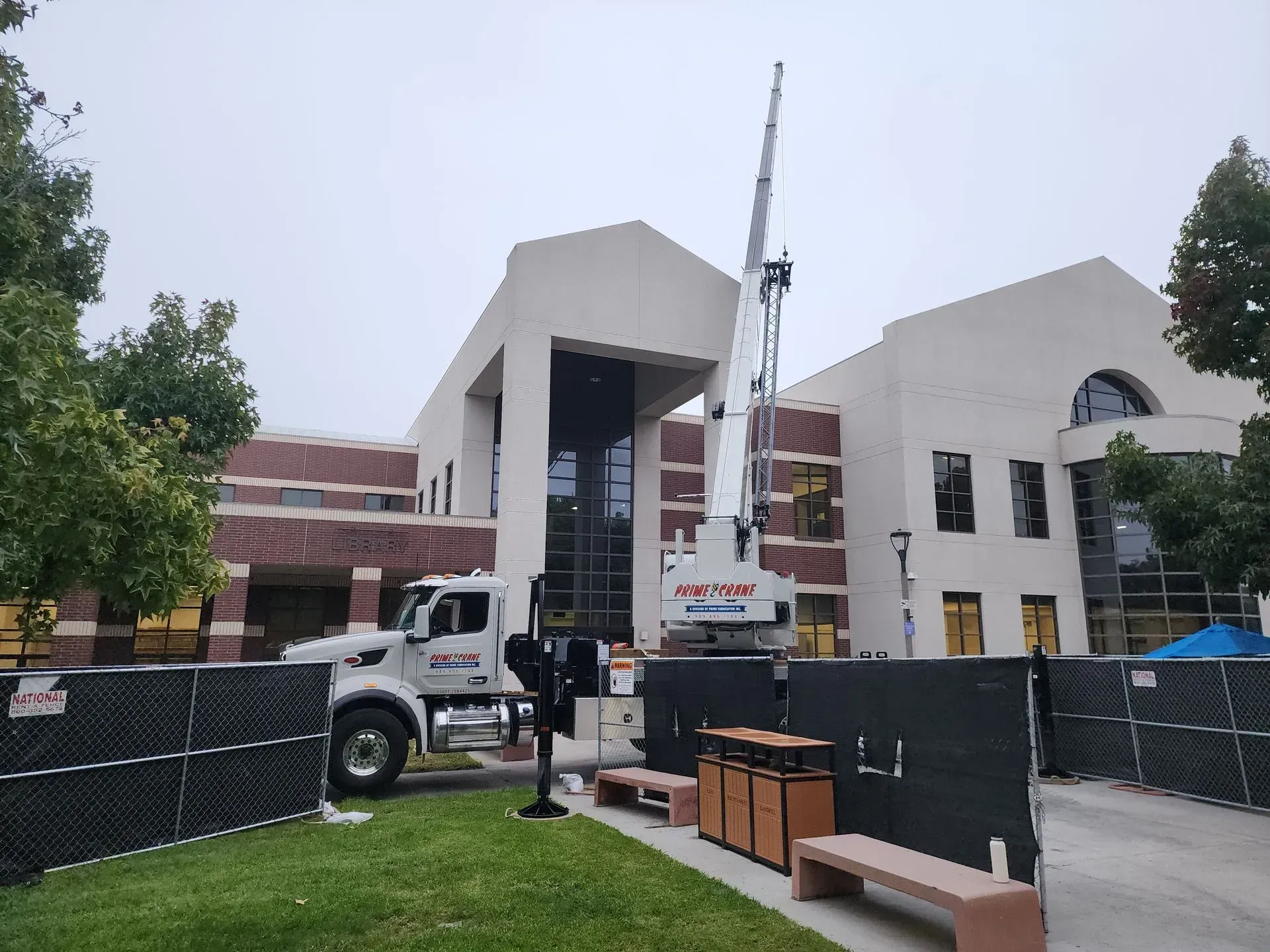A large crane near a beige building on a cloudy day, construction site with barriers.
