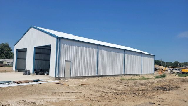 A large white building with blue trim is sitting in the middle of a dirt field.