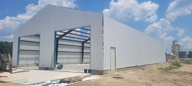 A large white metal building is being built in a field.