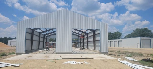 A large metal building is being built in the middle of a dirt field.